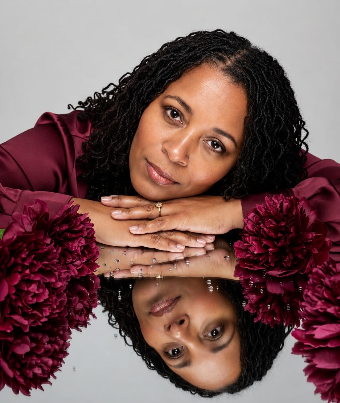 Sonya Narcisse, founder and Community Curator of Sister Soul Wellness, resting beside deep burgundy flowers